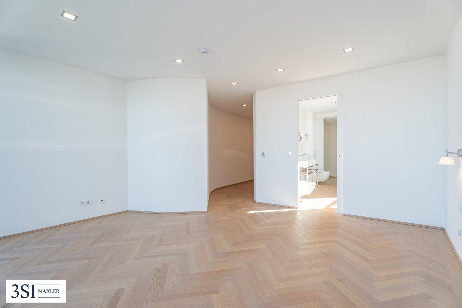 Geräumiges Schlafzimmer mit Fischgrätparkett und direktem Zugang zu einem modernen Badezimmer.