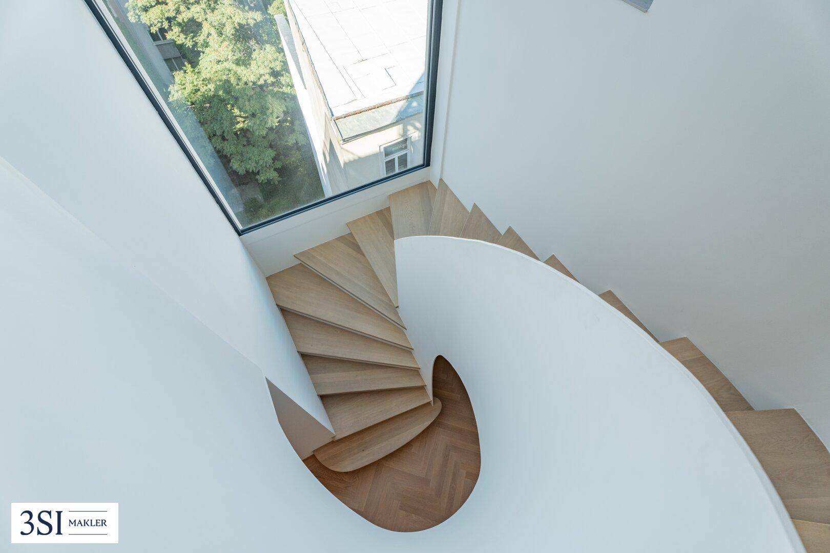 Elegante Wendeltreppe aus Holz mit einem großen Oberlicht, das den Bereich hell erleuchtet.