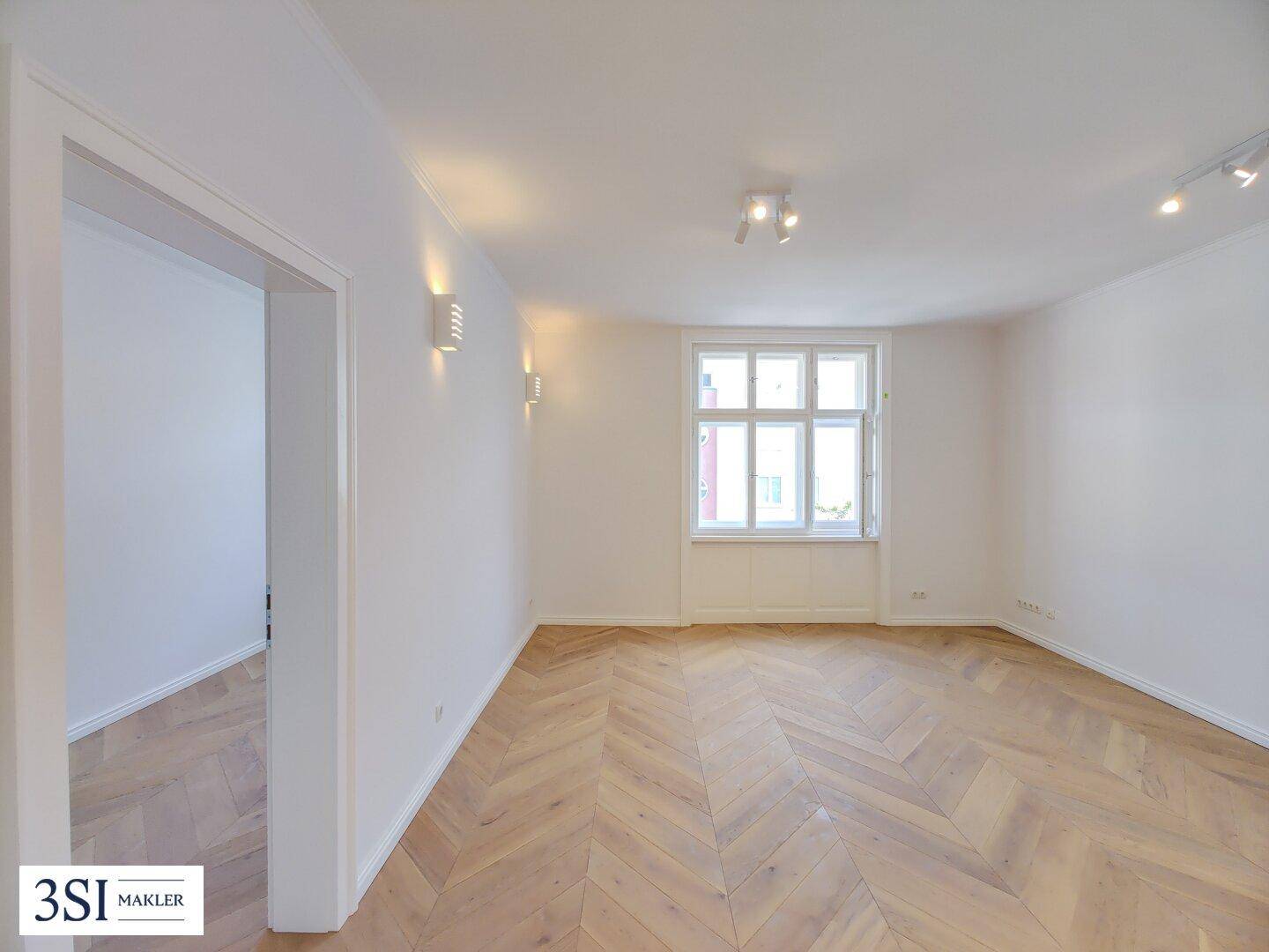 Geräumiger, heller Raum mit Fischgrätparkett und einem Fenster, das viel Tageslicht hereinlässt.