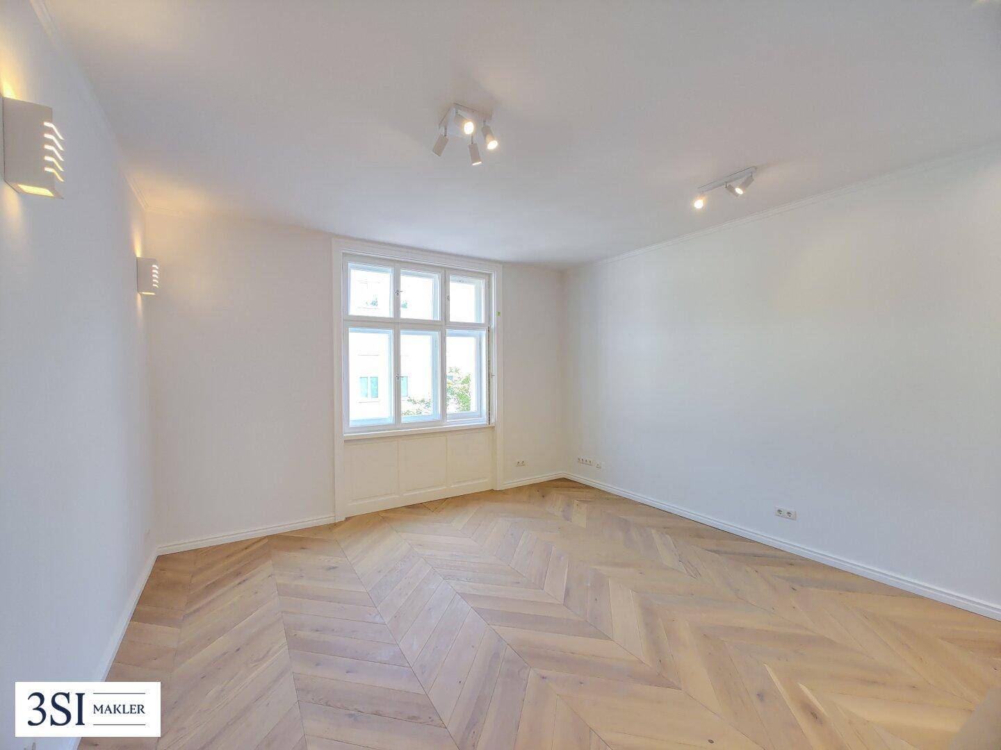 Heller Raum mit elegantem Fischgrätparkett, weißen Wänden und modernen Wandleuchten.