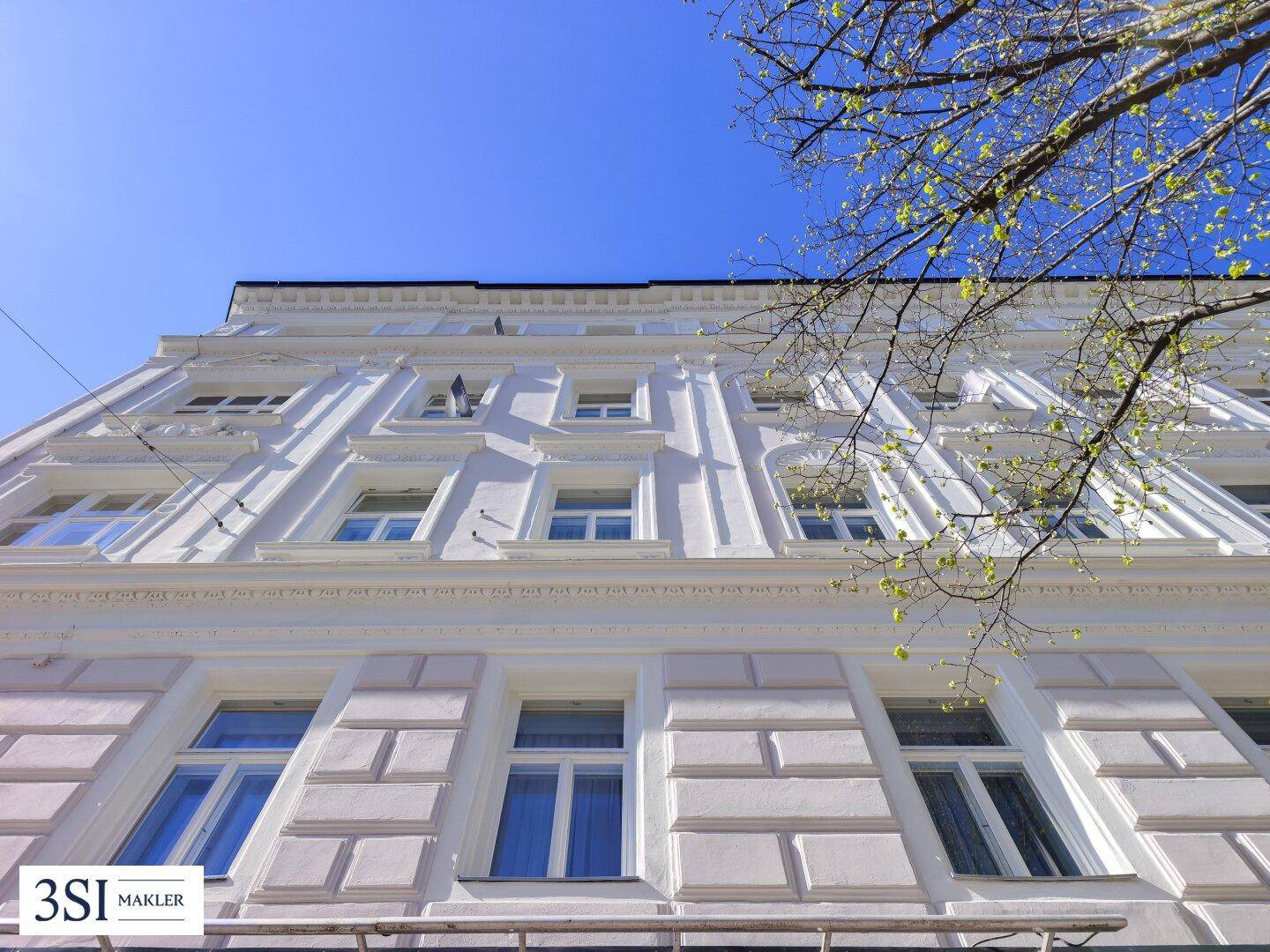 Detailansicht der historischen Fassade mit dekorativen Elementen und großen Fenstern.