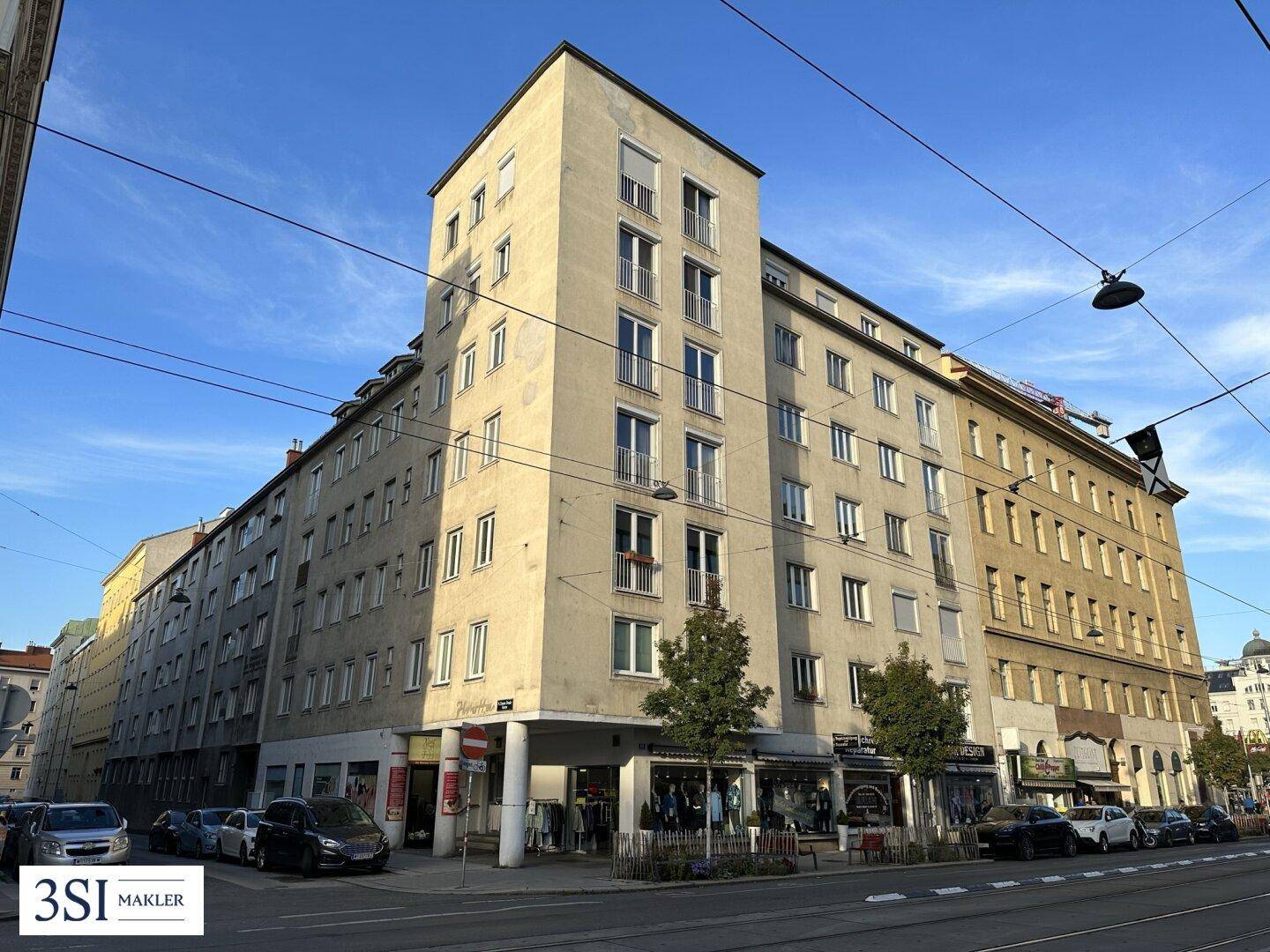 Mehrstöckiges Gebäude an einer belebten Straße mit Geschäften im Erdgeschoss und Wohnungen darüber.