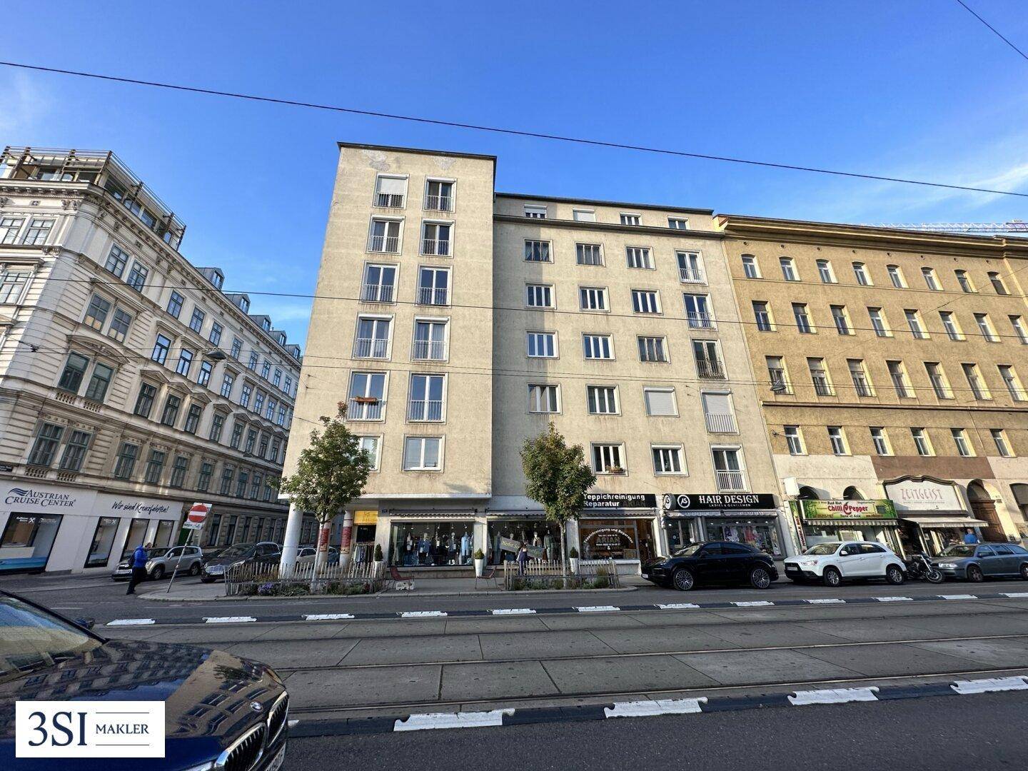 Gesamtansicht eines Gebäudekomplexes an einer städtischen Straße mit Geschäften und Wohnungen.
