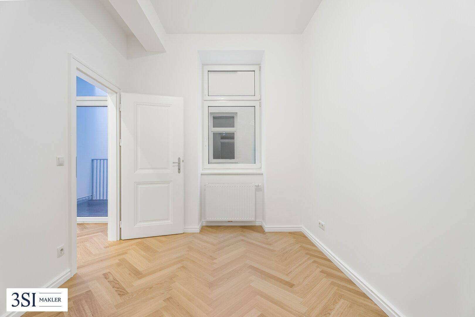 Helles Zimmer mit Fischgrätparkett und Zugang zu einem Balkon, bietet viel Tageslicht.