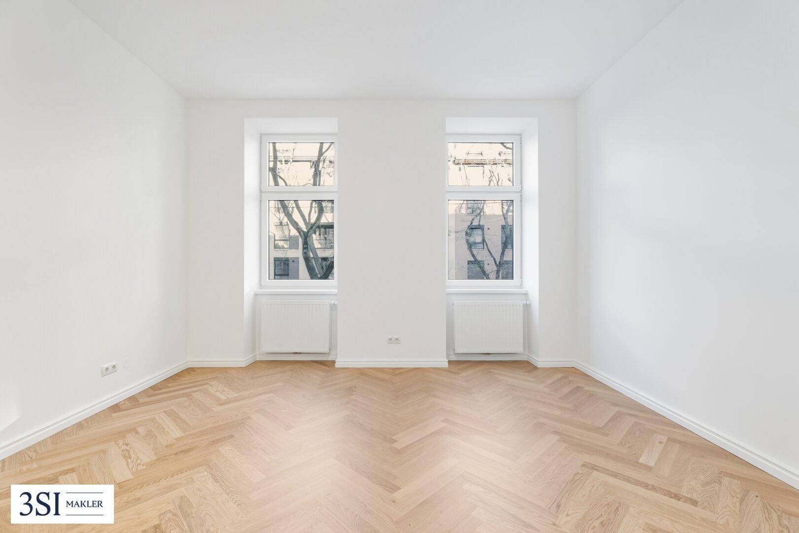 Geräumiges, helles Zimmer mit klassischem Fischgrätparkett und Blick nach draußen.