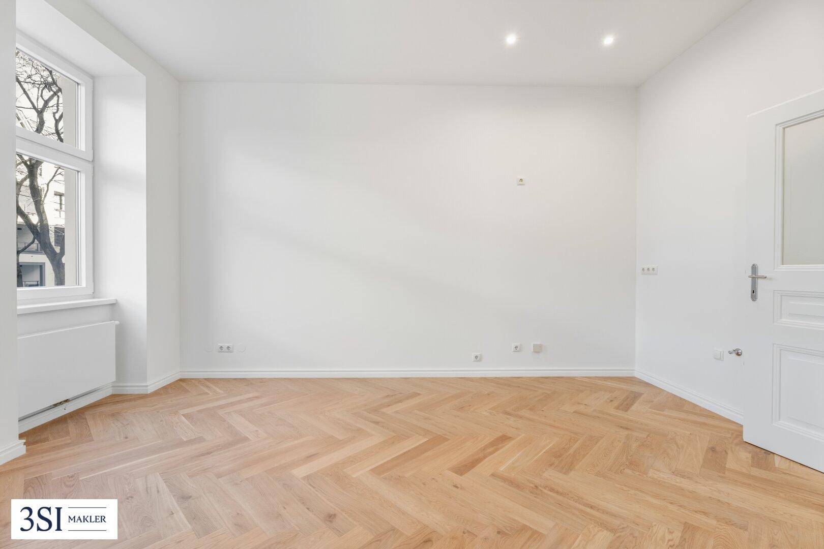 Lichtdurchfluteter Raum mit elegantem Fischgrätparkett und einer klassischen weißen Tür.
