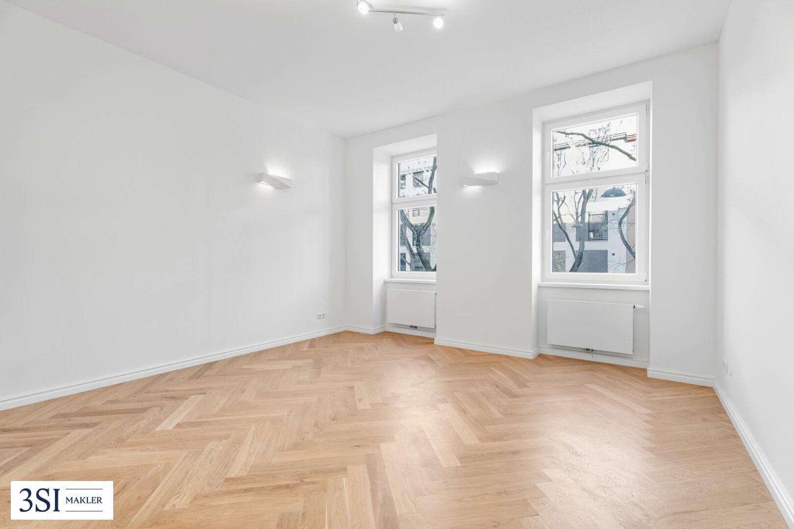 Geräumiges, helles Zimmer mit modernem Fischgrätparkett und Einbaustrahlern an der Decke.