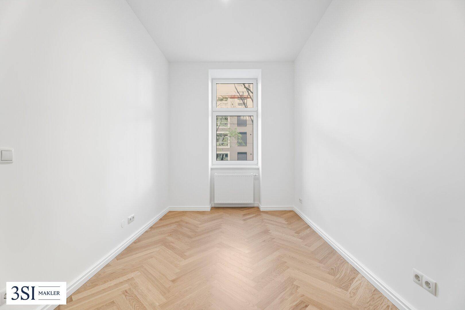 Kleineres, helles Zimmer mit Fischgrätparkett und einem Fenster, ideal als Schlaf- oder Arbeitszimmer.