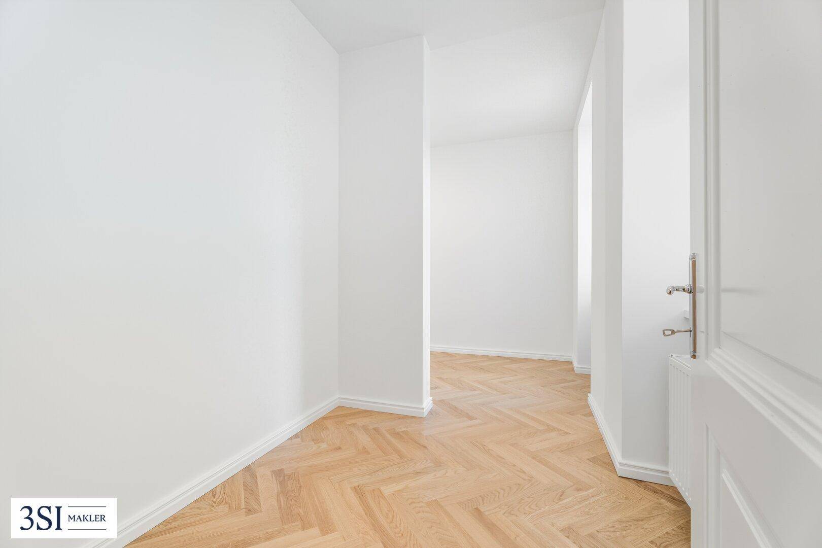 Langer, heller Flur mit Fischgrätparkett und weißer Tür, führt zu weiteren Wohnbereichen.