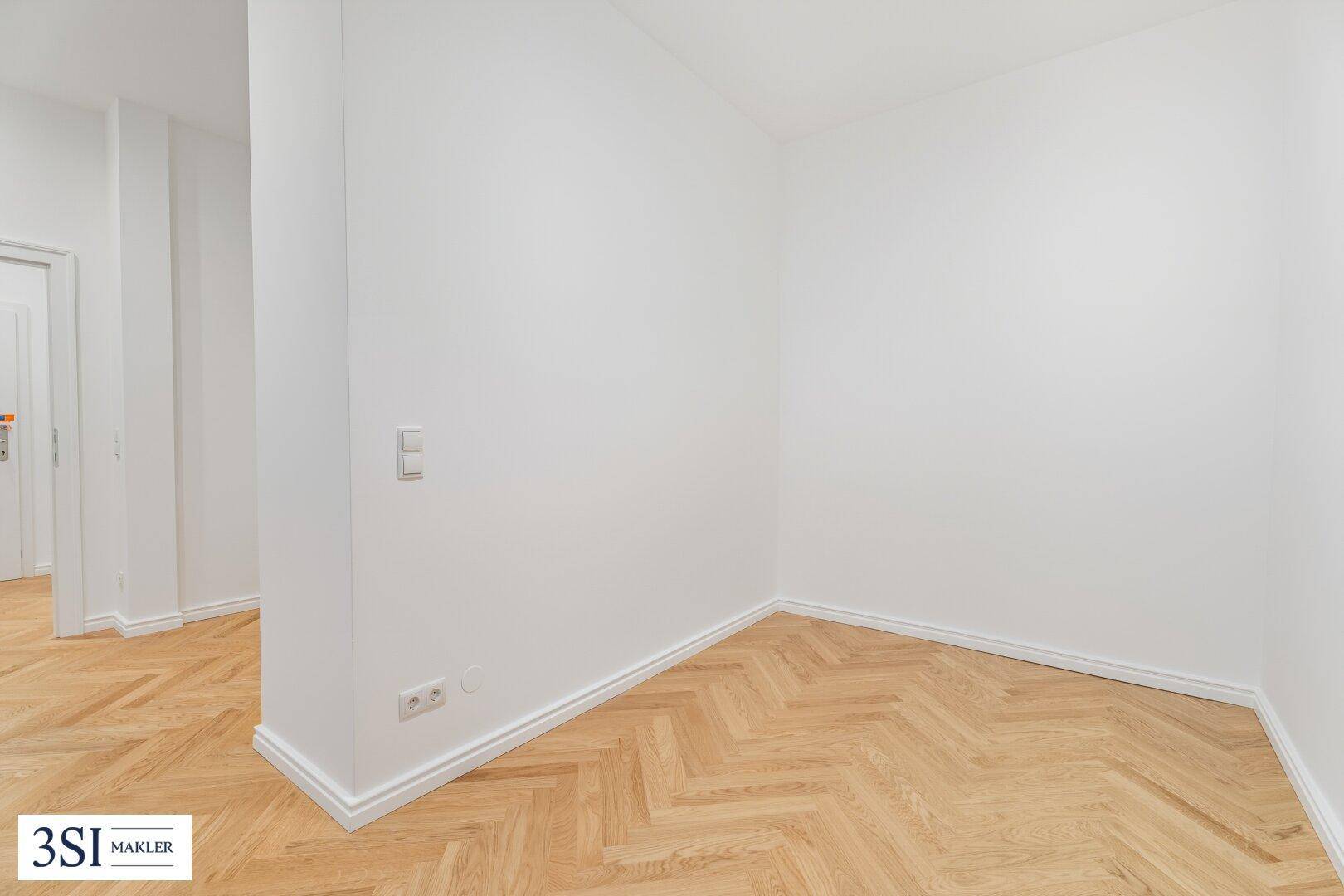 Heller Eckbereich mit Fischgrätparkett und weißen Wänden, ideal für einen Flur.