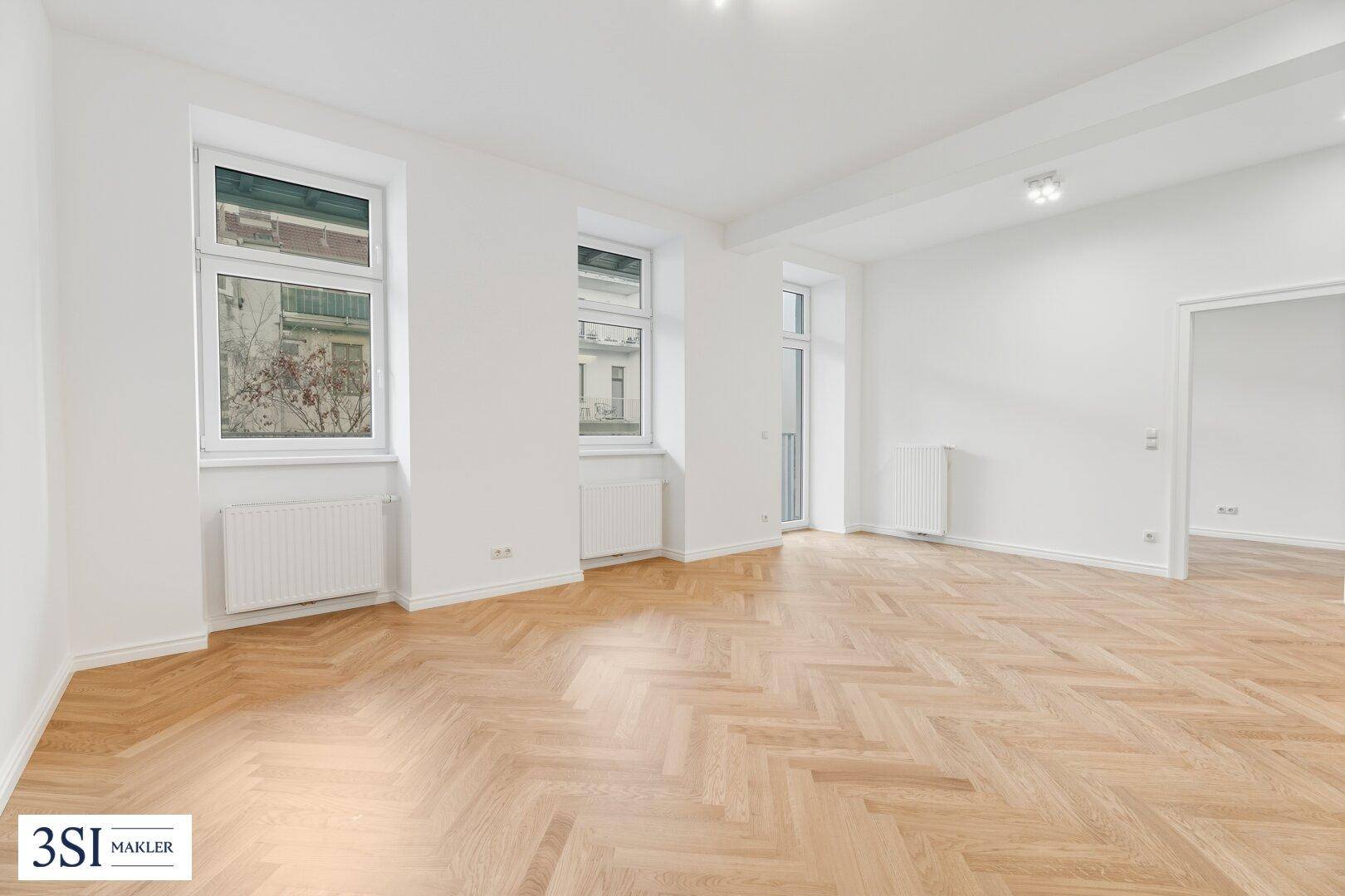 Geräumiges Wohnzimmer mit hellem Fischgrätparkett, weißen Wänden und moderner Deckenbeleuchtung.