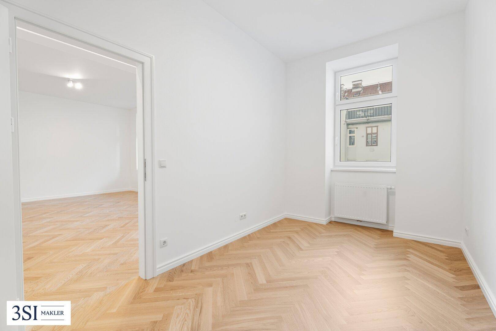 Kleineres Zimmer mit Fischgrätparkett und einem Fenster mit Blick auf die Umgebung.