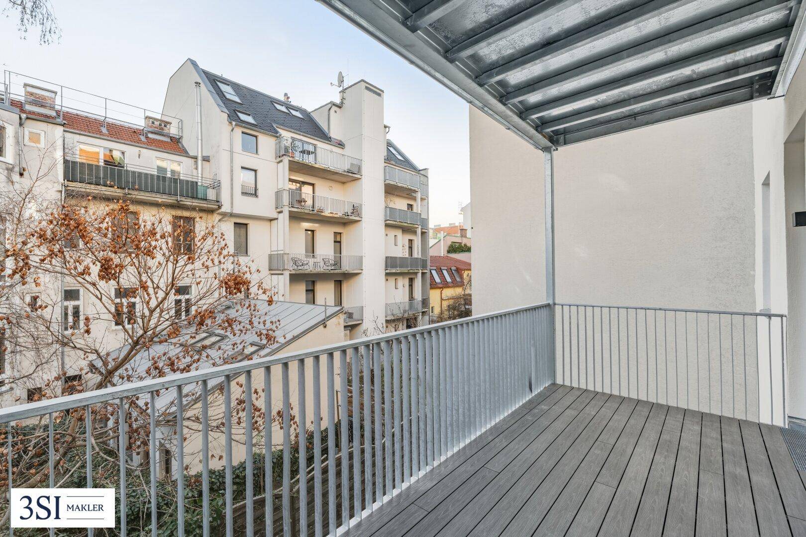 Geräumiger Balkon mit Holzboden und Blick auf den Innenhof und umliegende Gebäude.