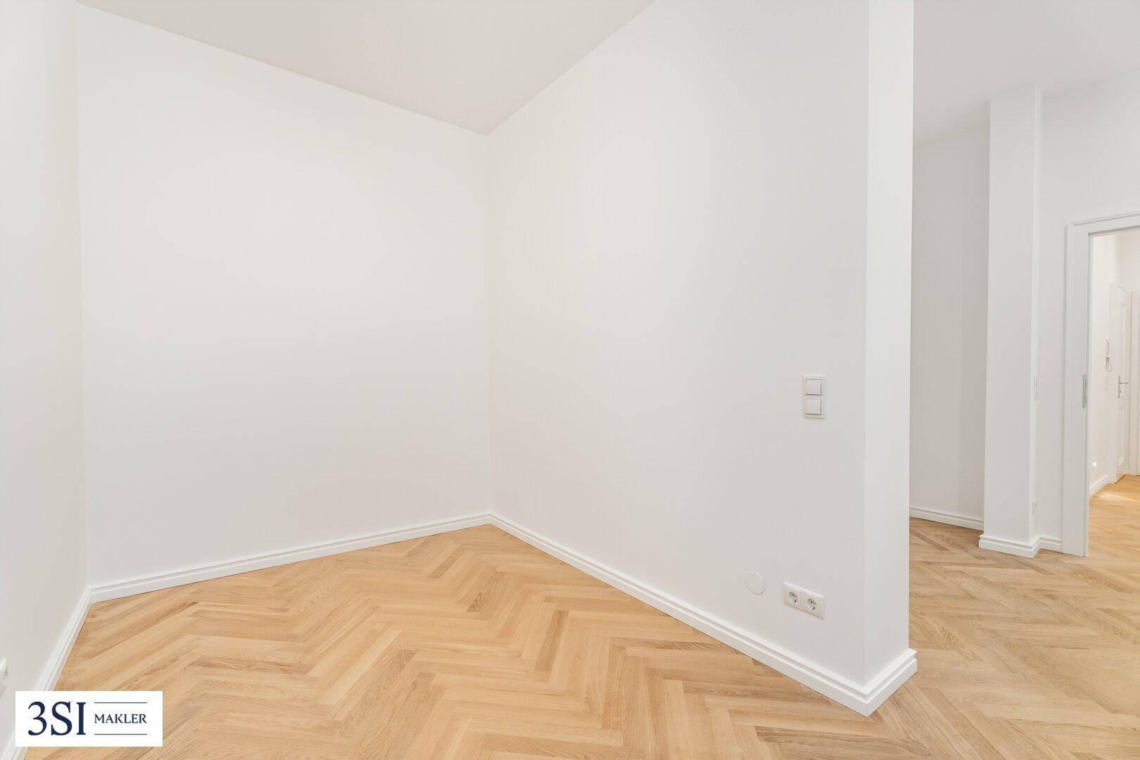 Heller Flurbereich mit Fischgrätparkett und weißen Wänden, der zu weiteren Räumen führt.