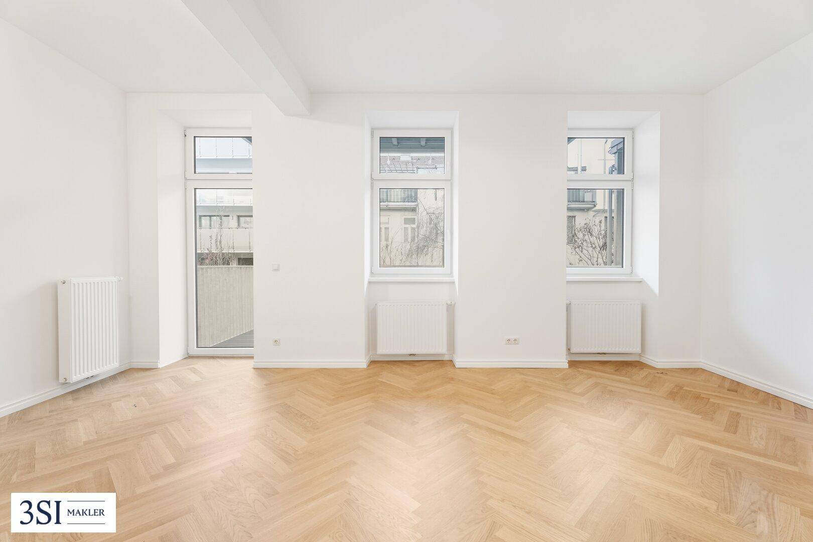 Lichtdurchfluteter Raum mit elegantem Fischgrätparkett und Zugang zu einem französischen Balkon.