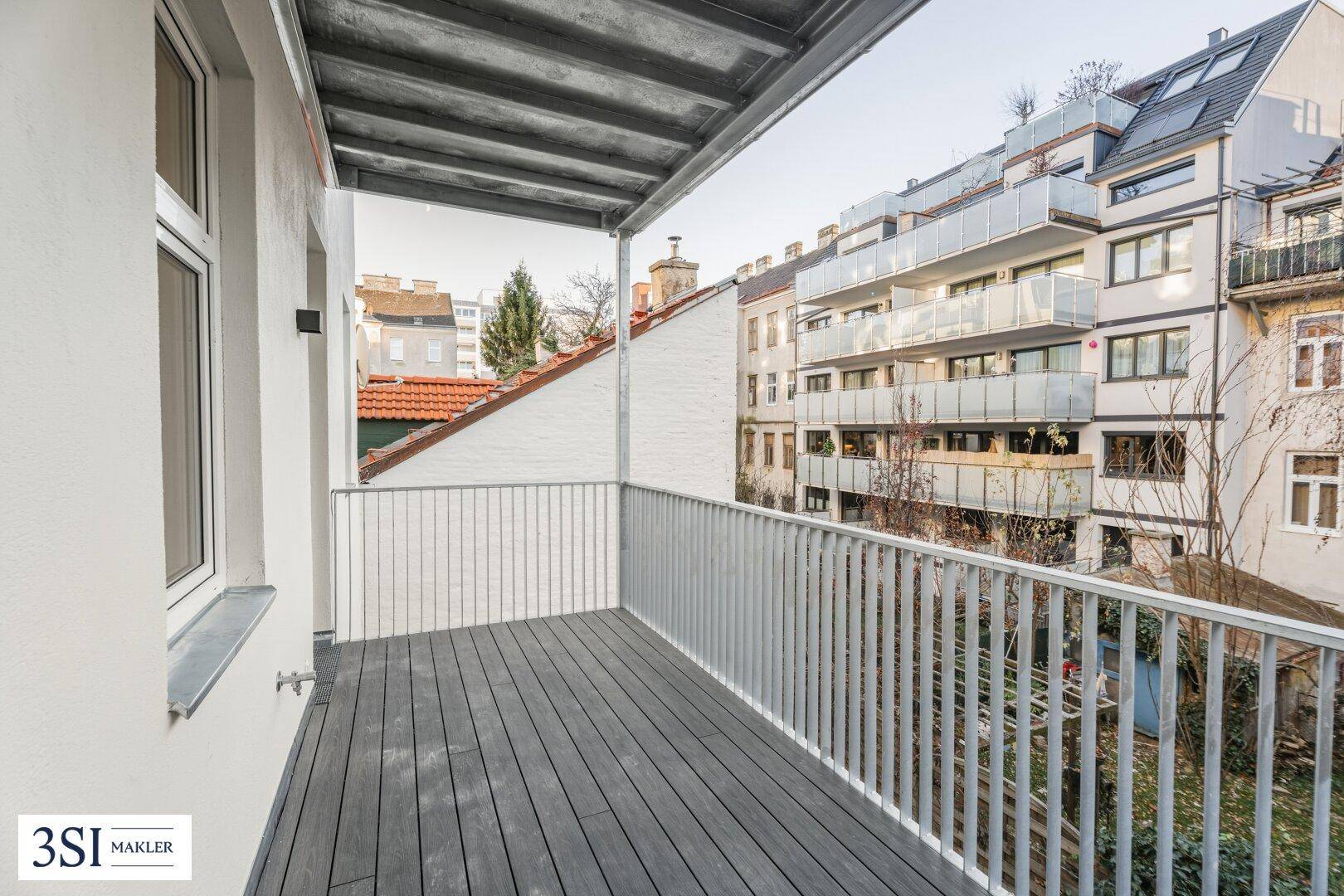 Geräumiger Balkon mit Holzboden und Blick auf die umliegenden Gebäude und den Himmel.