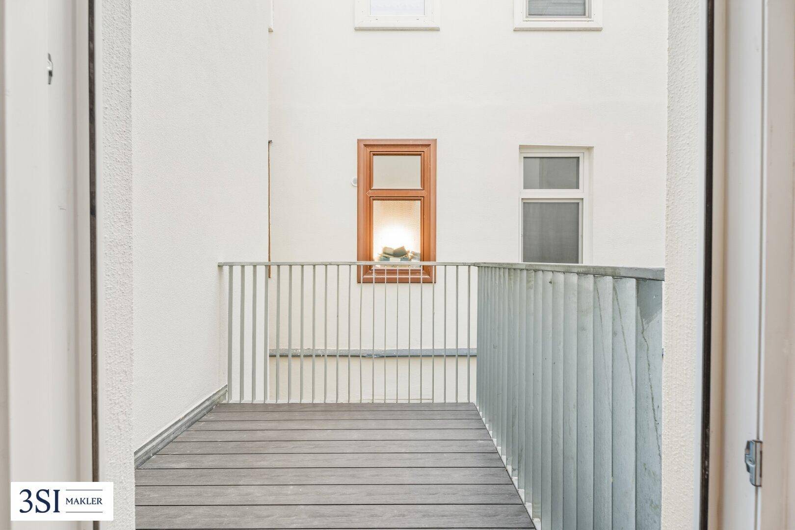 Kleiner Balkon mit Holzbelag und Metallgeländer, der einen Blick auf den Innenhof bietet.