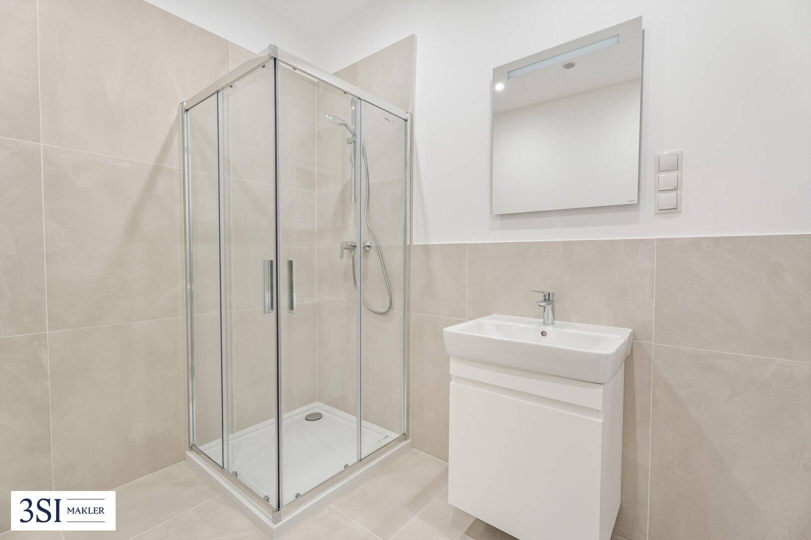 Modernes Badezimmer mit Duschkabine, Waschbecken und hellen, großformatigen Fliesen.