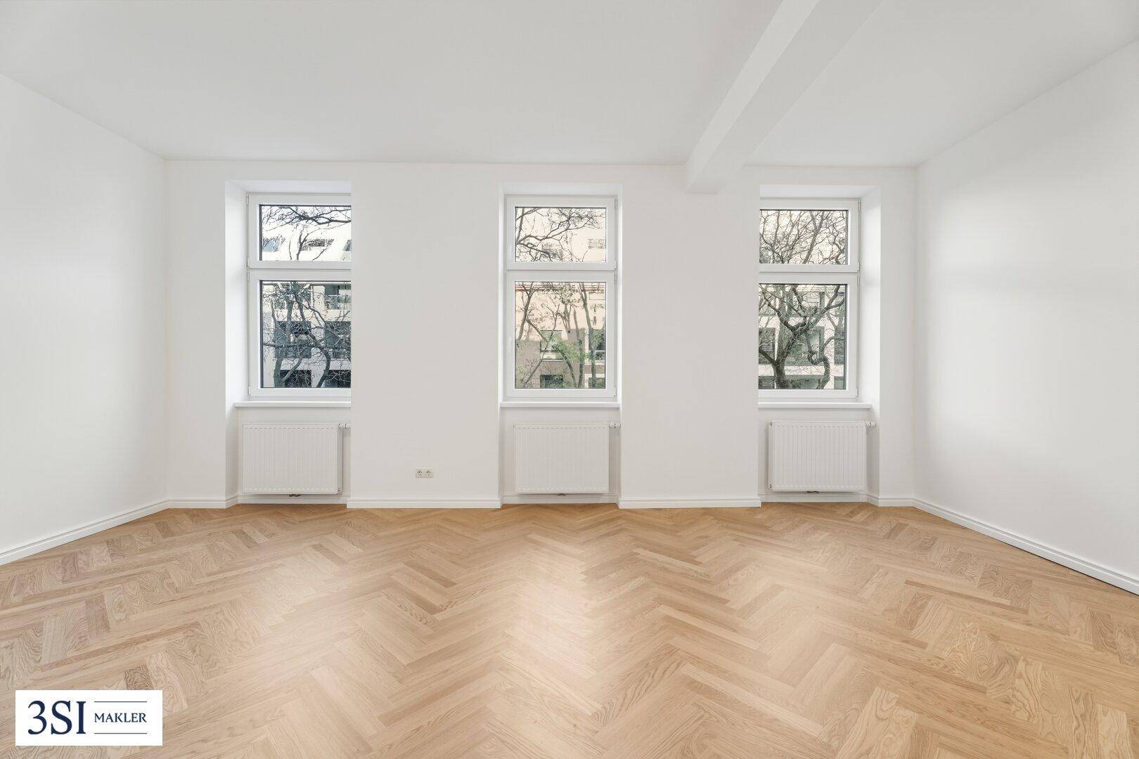 Geräumiges, helles Wohnzimmer mit klassischem Fischgrätparkett und Blick ins Grüne.