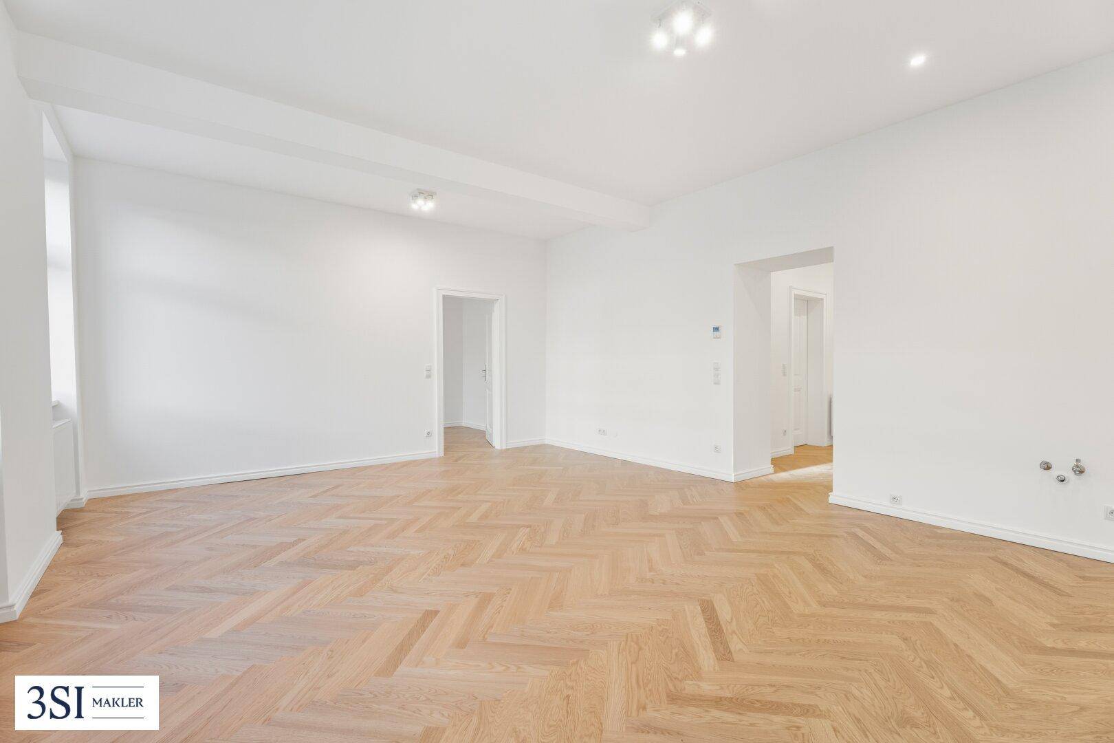 Weitläufiges Wohnzimmer mit Fischgrätparkett und Zugang zu weiteren Räumen, frisch renoviert.