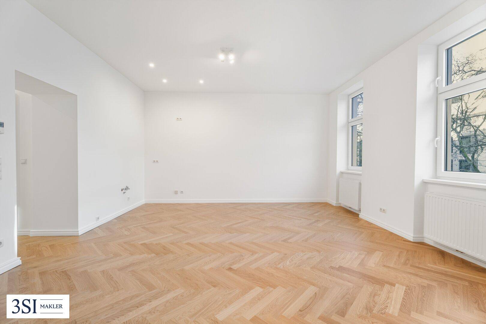 Lichtdurchflutetes Wohnzimmer mit neuem Fischgrätparkett und Blick auf die umliegenden Bäume.