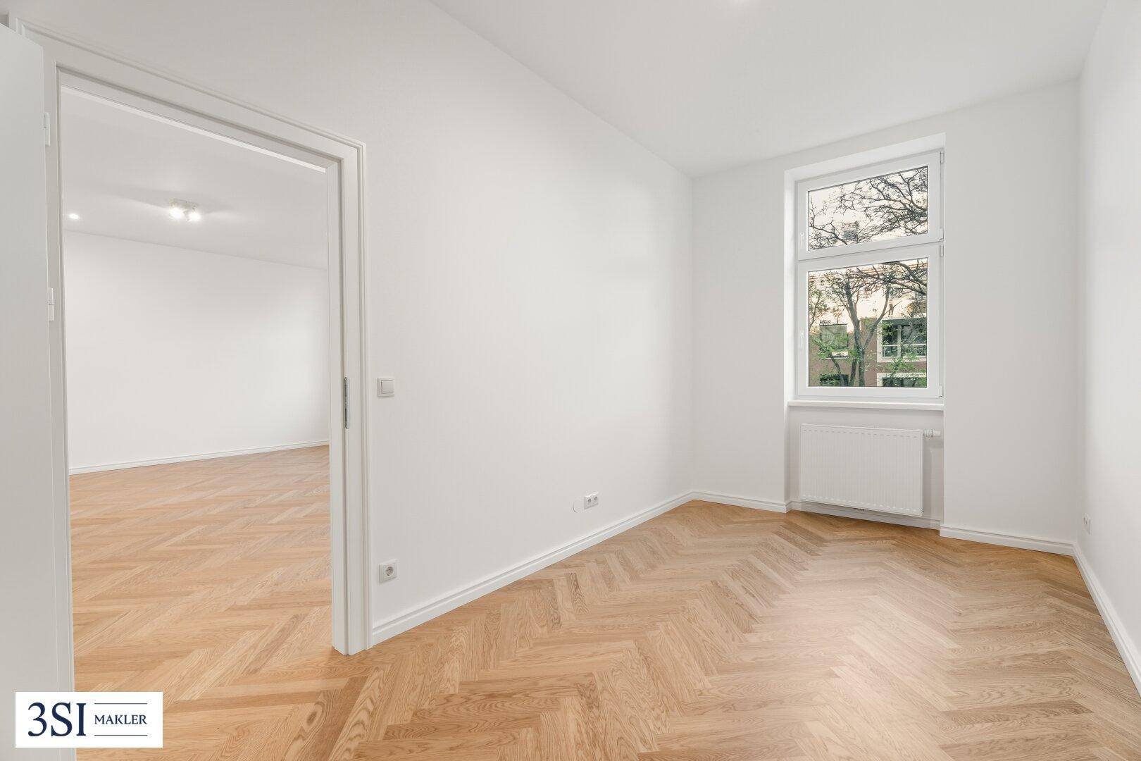 Ruhiges Zimmer mit Fischgrätparkett und einem Fenster, das eine grüne Aussicht bietet.