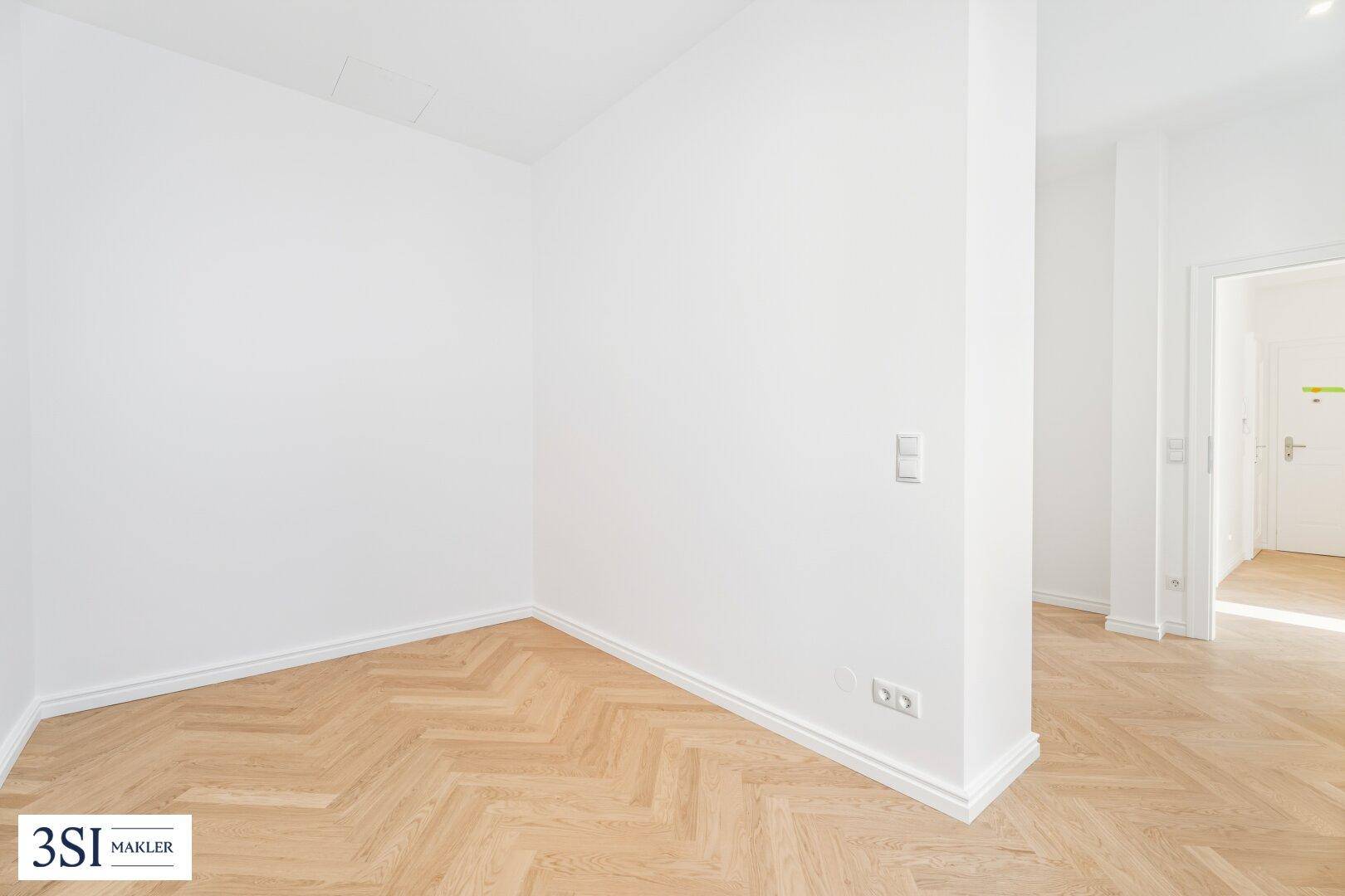 Heller Eckbereich mit Fischgrätparkett und weiß gestrichenen Wänden, der einen Übergang bildet.