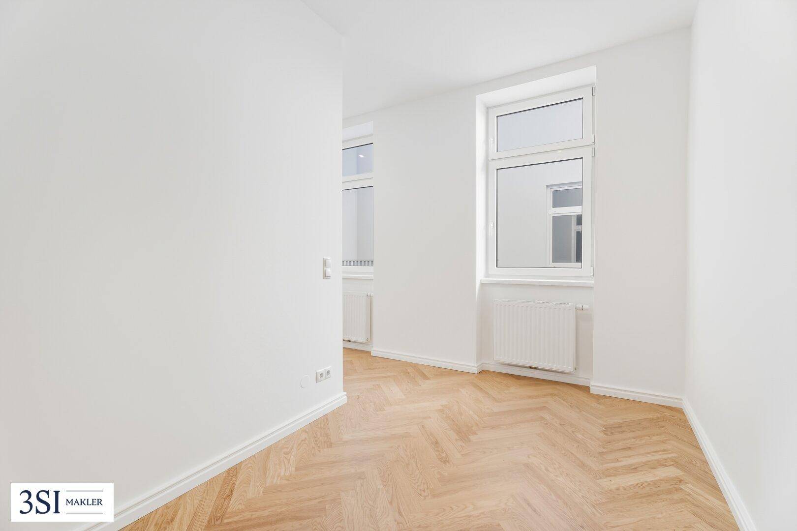 Lichtdurchflutetes Zimmer mit Fischgrätparkett und zwei Fenstern, ideal für Wohn- oder Arbeitsbereich.