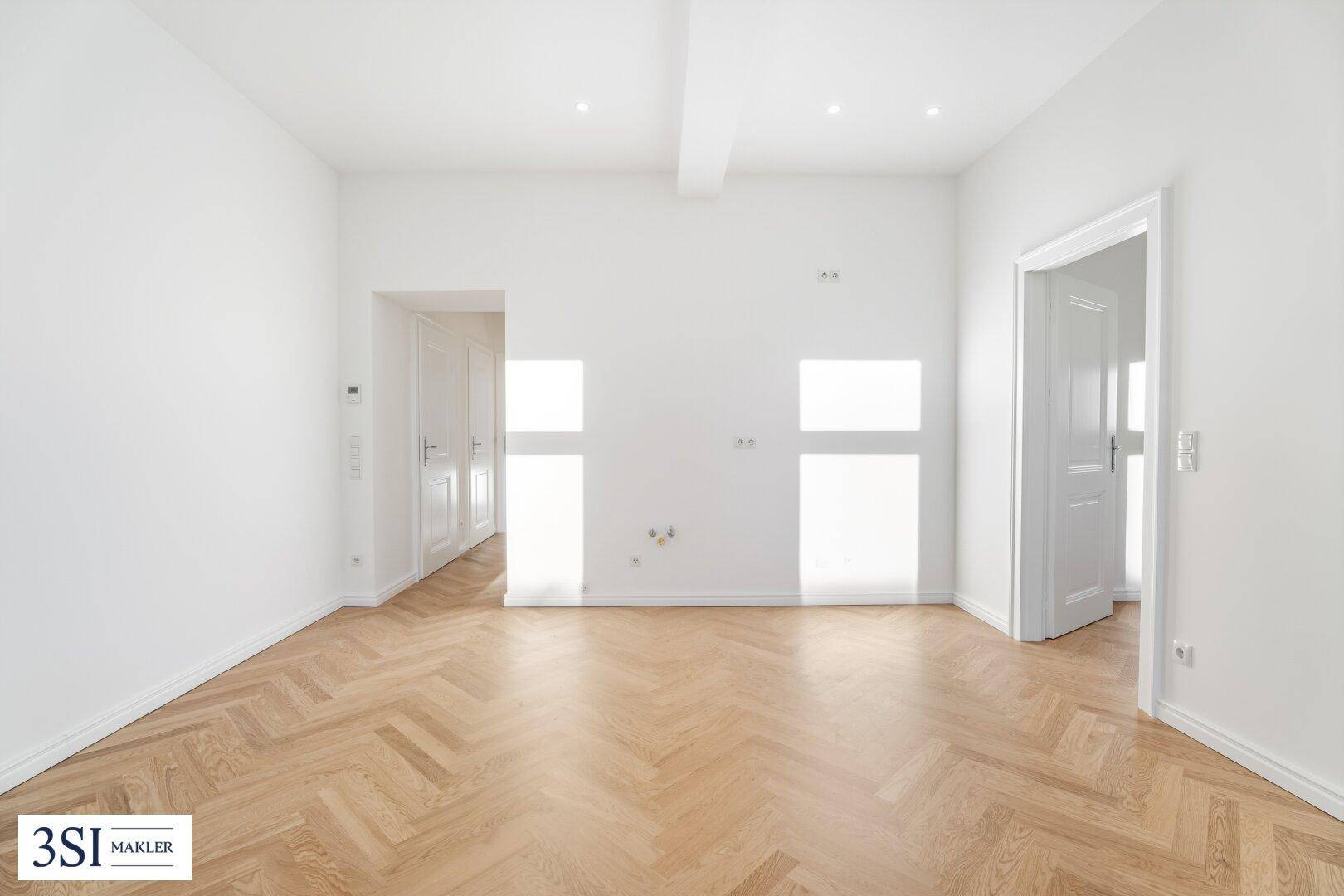 Geräumiges, helles Zimmer mit Fischgrätparkett und weiß gestrichenen Wänden.