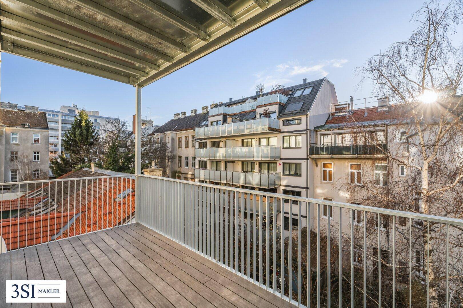 Geräumiger Balkon mit Holzboden und Blick auf die umliegenden Gebäude und den Himmel.