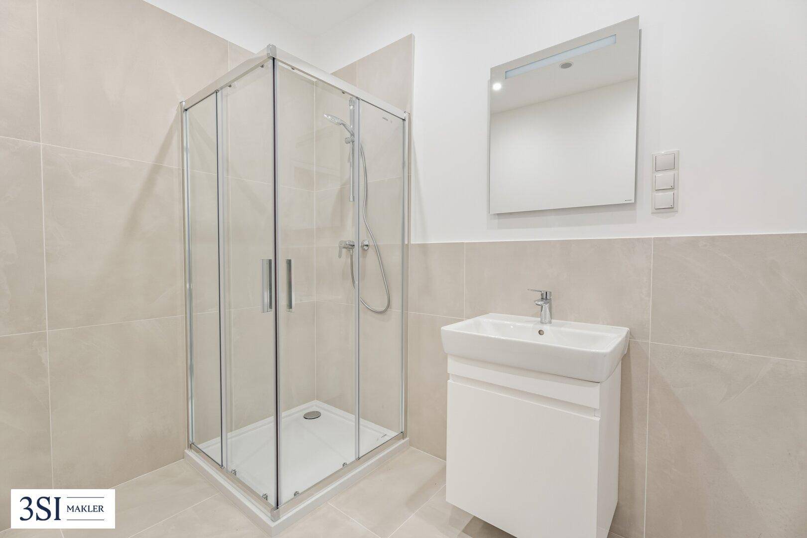 Modernes Badezimmer mit Duschkabine, Waschbecken und hellen Fliesen an Wänden und Boden.