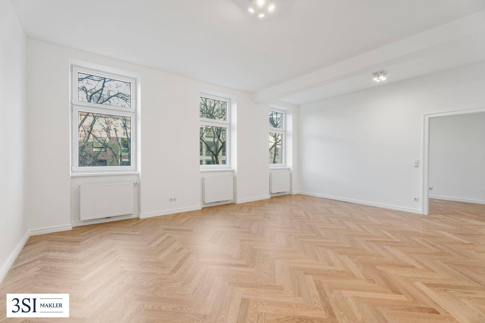 Lichtdurchfluteter Wohnbereich mit elegantem Fischgrätparkett und Zugang zu einem weiteren Zimmer.