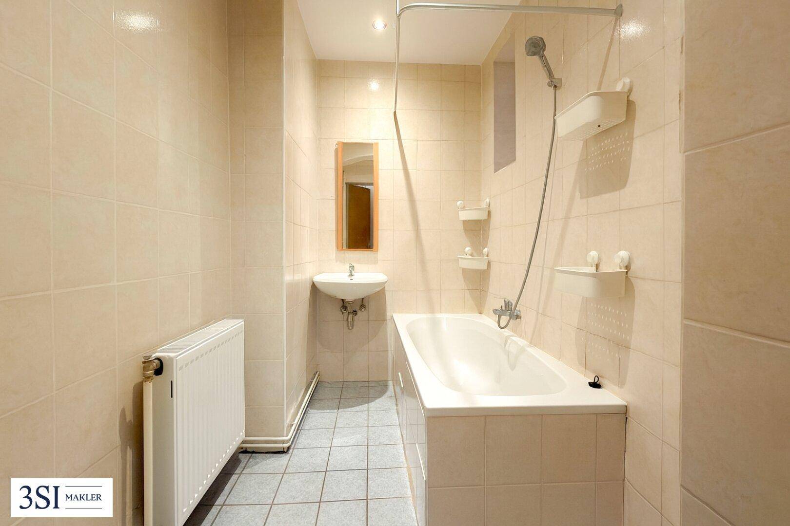 Gefliestes Badezimmer mit Badewanne, Waschbecken und Heizkörper, in gutem, aber älterem Zustand.