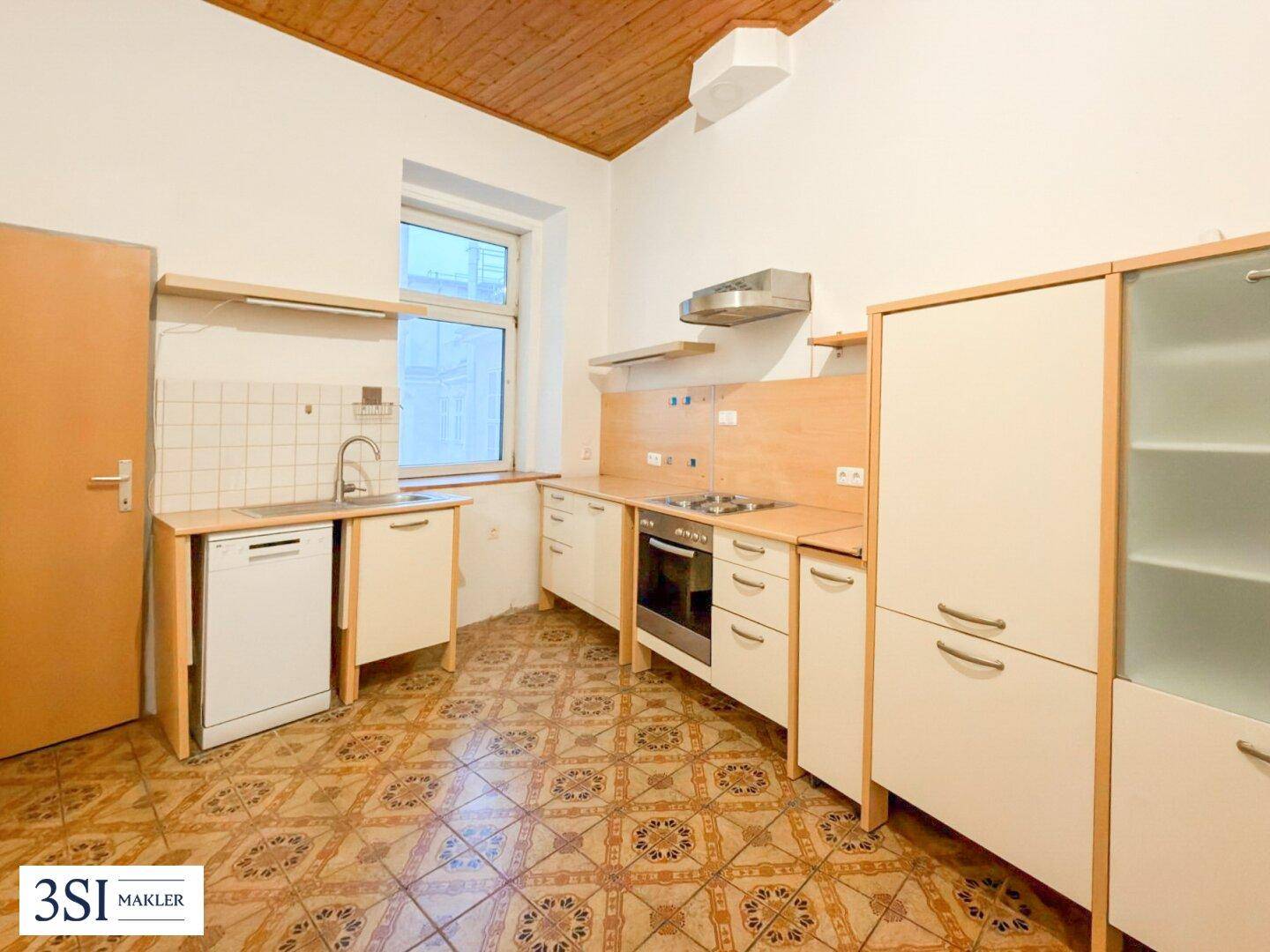 Funktionale Küche mit älteren Einbaumöbeln, Fliesenboden und Fenster, bereit zur Modernisierung.