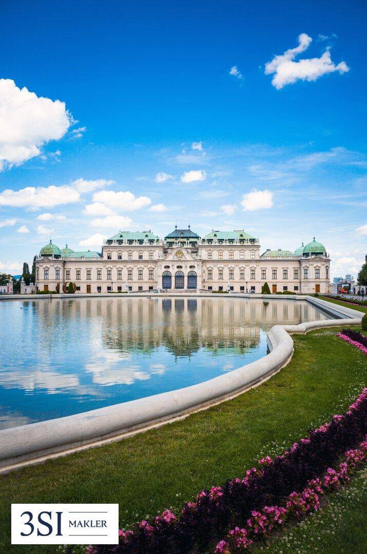 Majestätisches Schloss mit weitläufigen Gärten und einem großen Teich unter blauem Himmel.