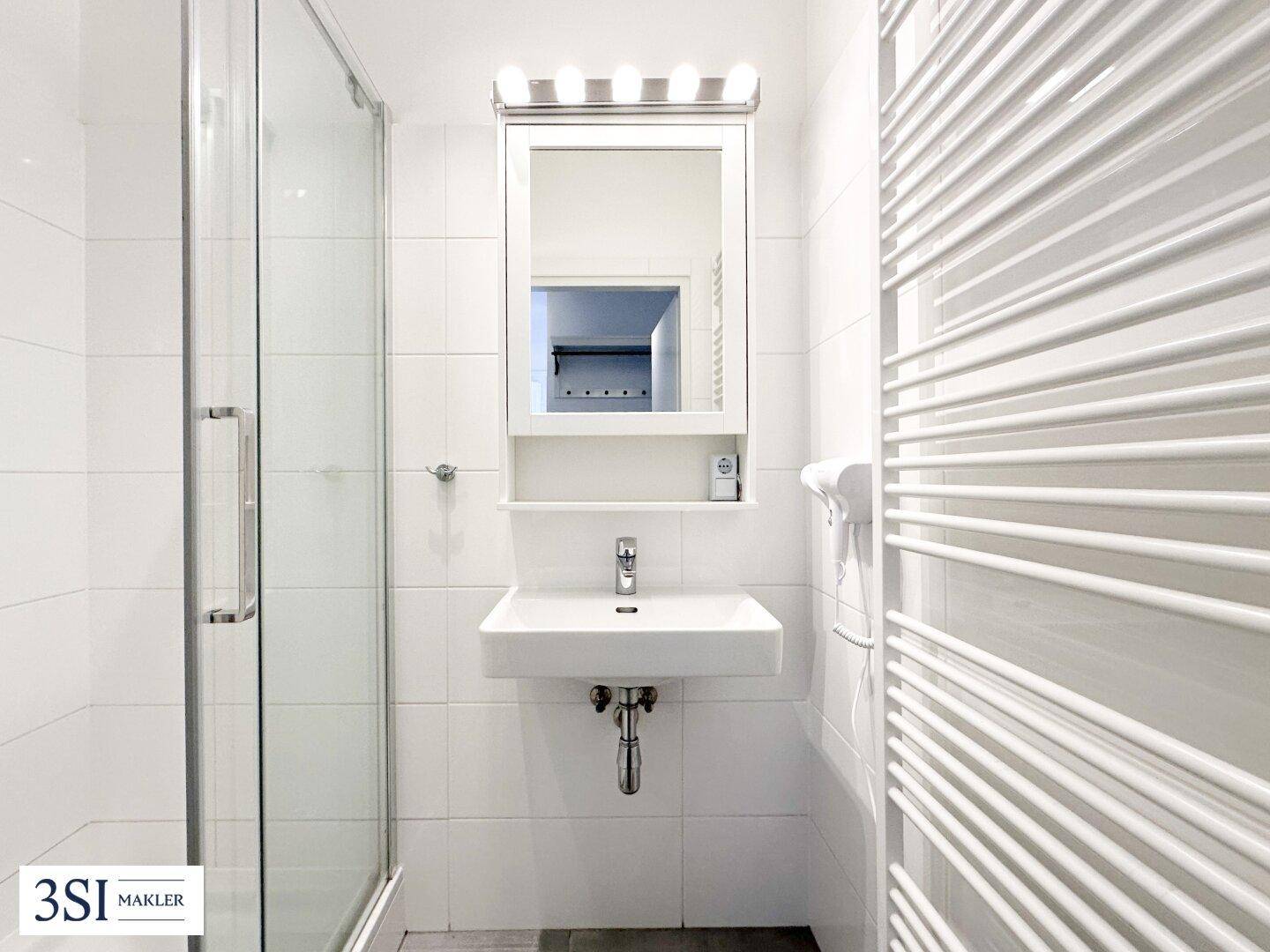 Helles Badezimmer mit Dusche, Waschbecken, Spiegelschrank und beheiztem Handtuchhalter.