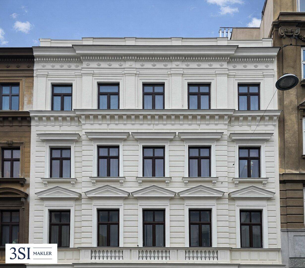 Klassische Altbaufassade mit symmetrischen Fenstern und einem kleinen Balkon im Erdgeschoss.