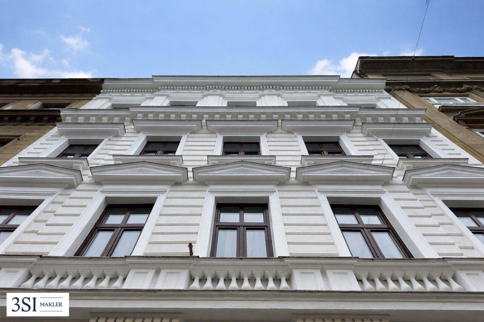 Historische Fassade eines Gebäudes mit klassischer Architektur und vielen Fenstern von unten betrachtet.