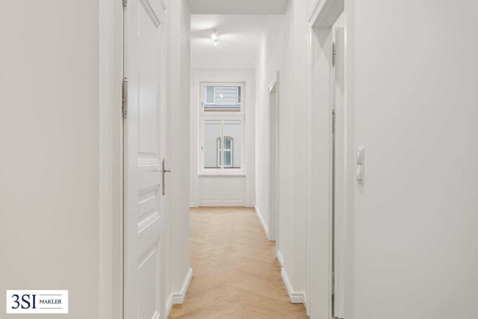 Langer, heller Flur mit Fischgrätparkett, der zu den verschiedenen Zimmern der Wohnung führt.