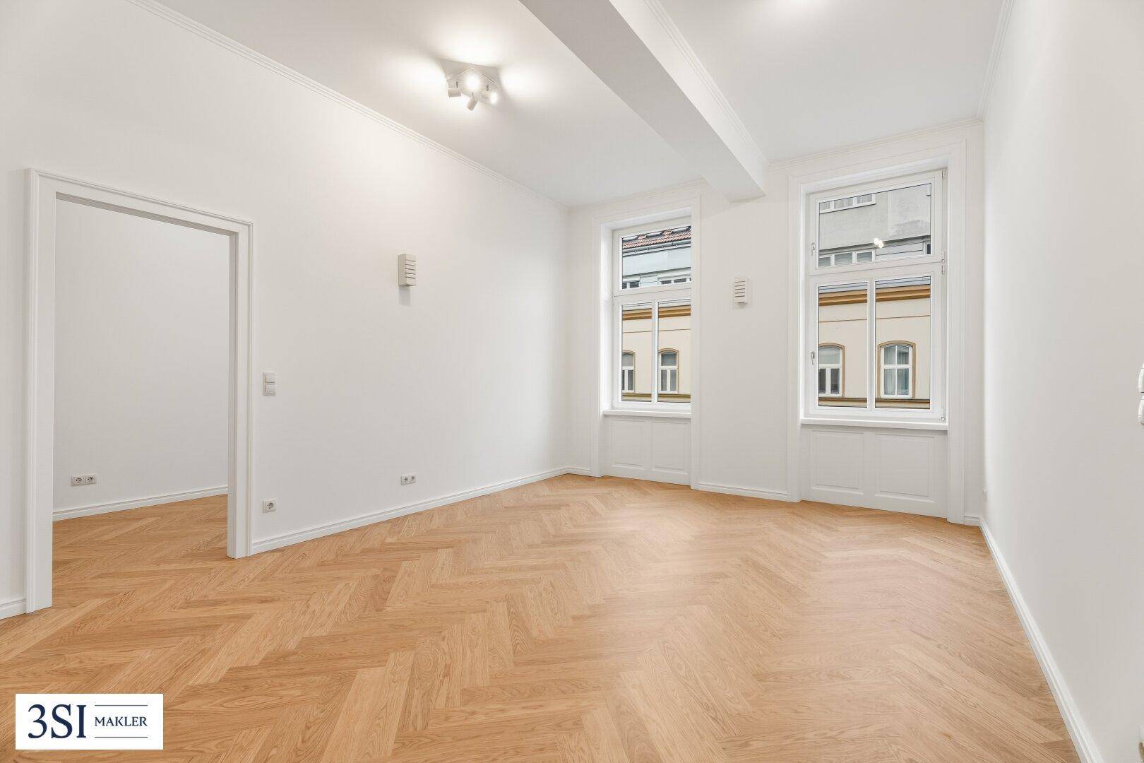 Geräumiges Zimmer mit hellem Fischgrätparkett und viel Tageslicht durch große Fenster.