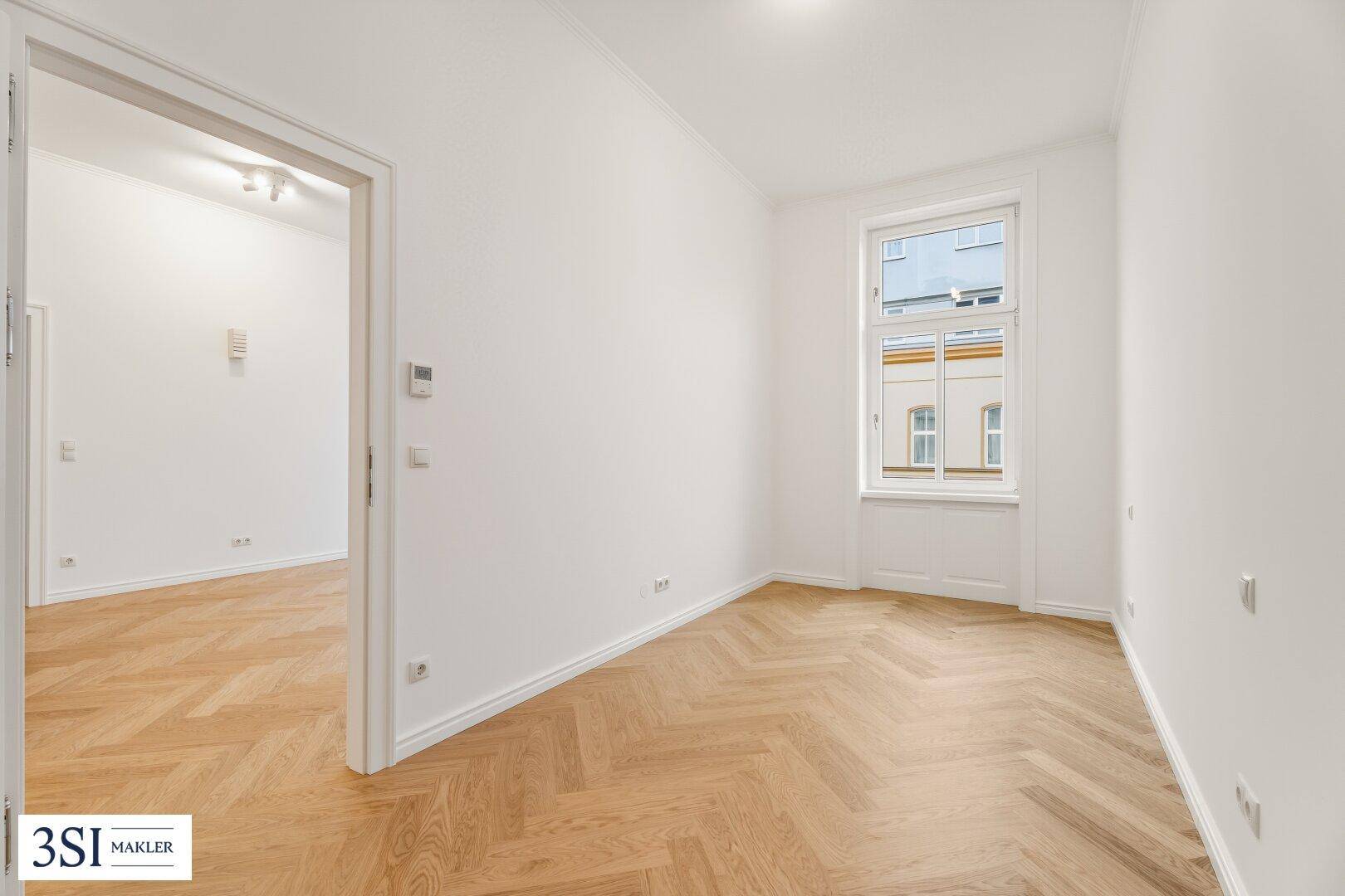 Gemütliches Zimmer mit hellem Fischgrätparkett und Blick auf die umliegenden Gebäude.