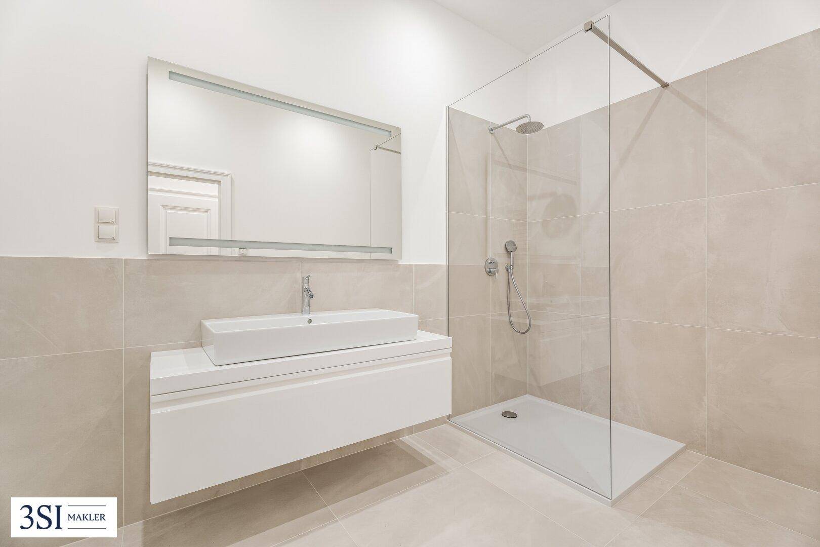 Modernes Badezimmer mit begehbarer Dusche, großem Spiegel und eleganten beigefarbenen Fliesen.