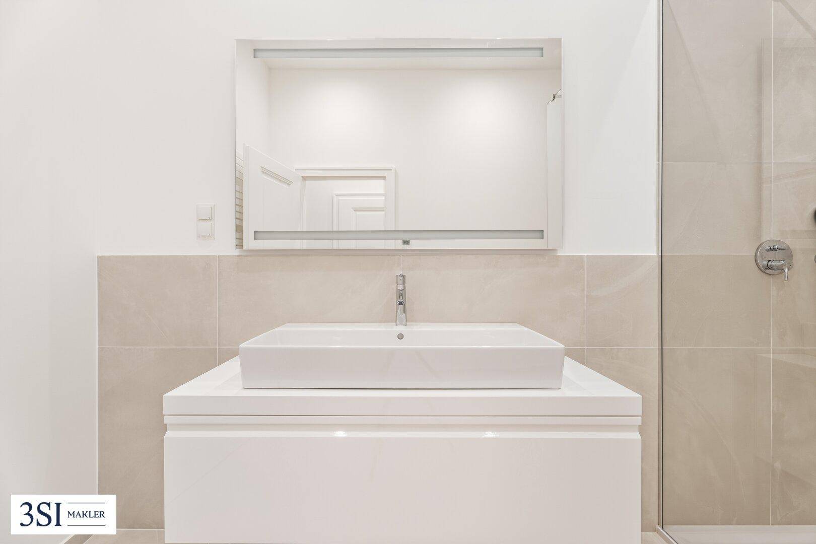 Detailansicht des modernen Waschtischs mit Aufsatzbecken und beleuchtetem Wandspiegel.