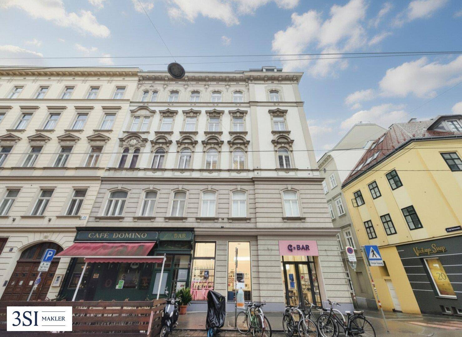Klassische Fassade eines Altbaus mit Geschäften im Erdgeschoss und Fahrrädern auf dem Bürgersteig.