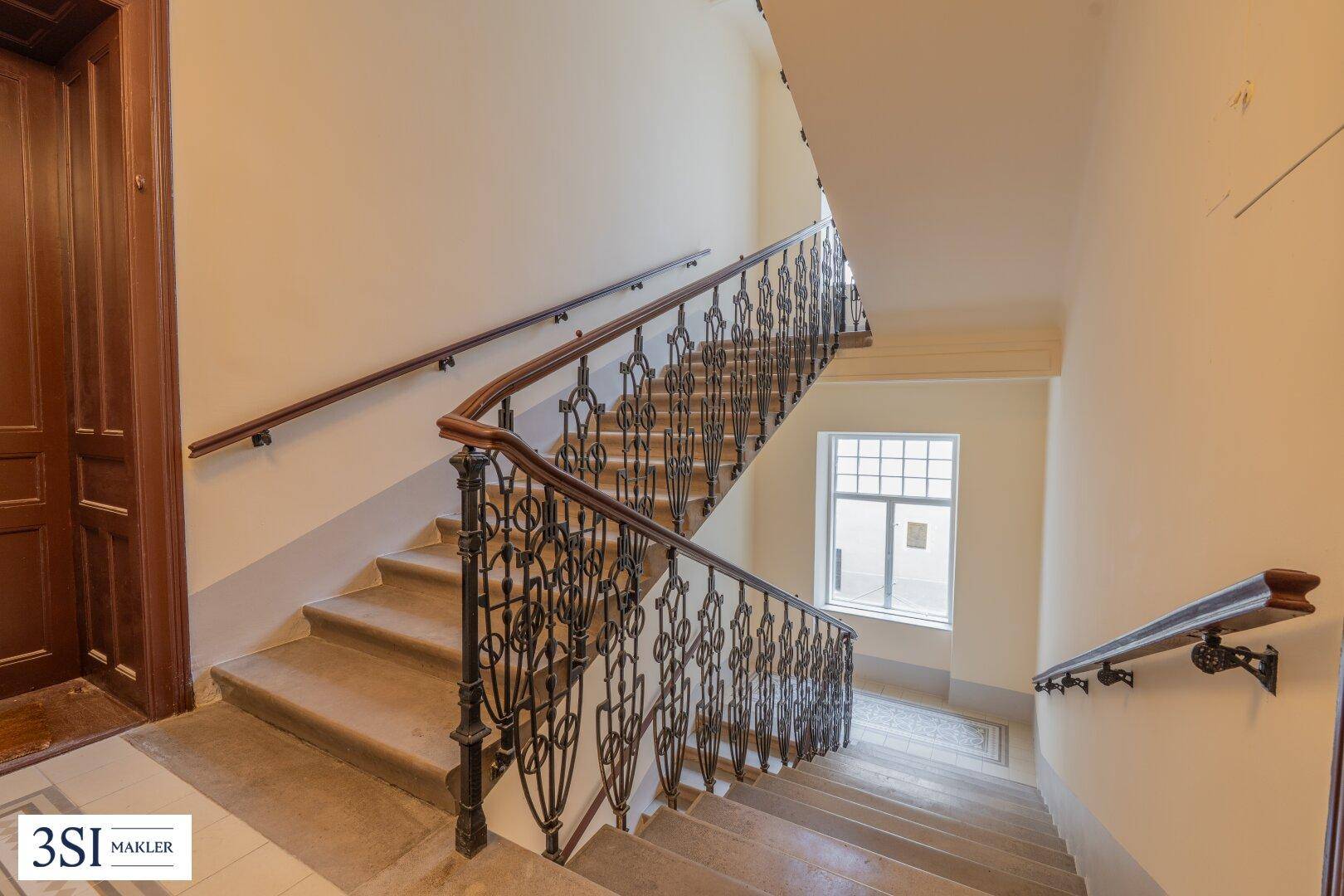 Historisches Treppenhaus mit kunstvoll geschmiedetem Geländer und großen Fenstern für natürliches Licht.