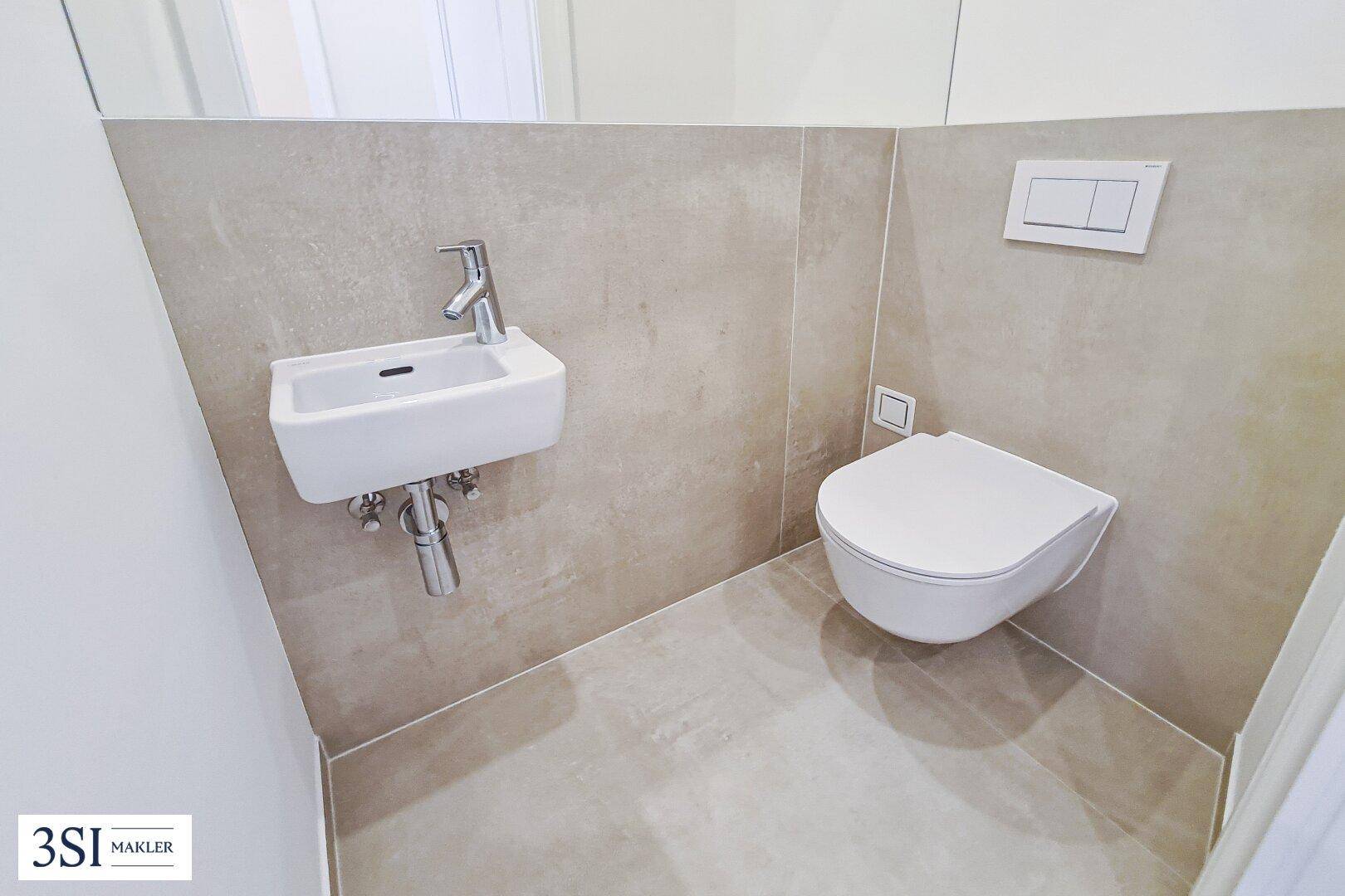 Modernes Gäste-WC mit wandmontierter Toilette und kleinem Waschbecken in neutralen Fliesen.