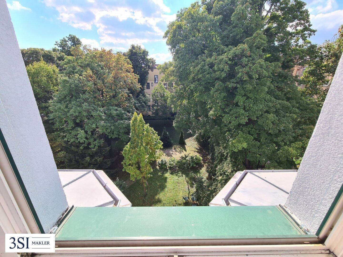 Blick aus dem Fenster auf einen grünen Innenhof mit vielen Bäumen und Pflanzen.