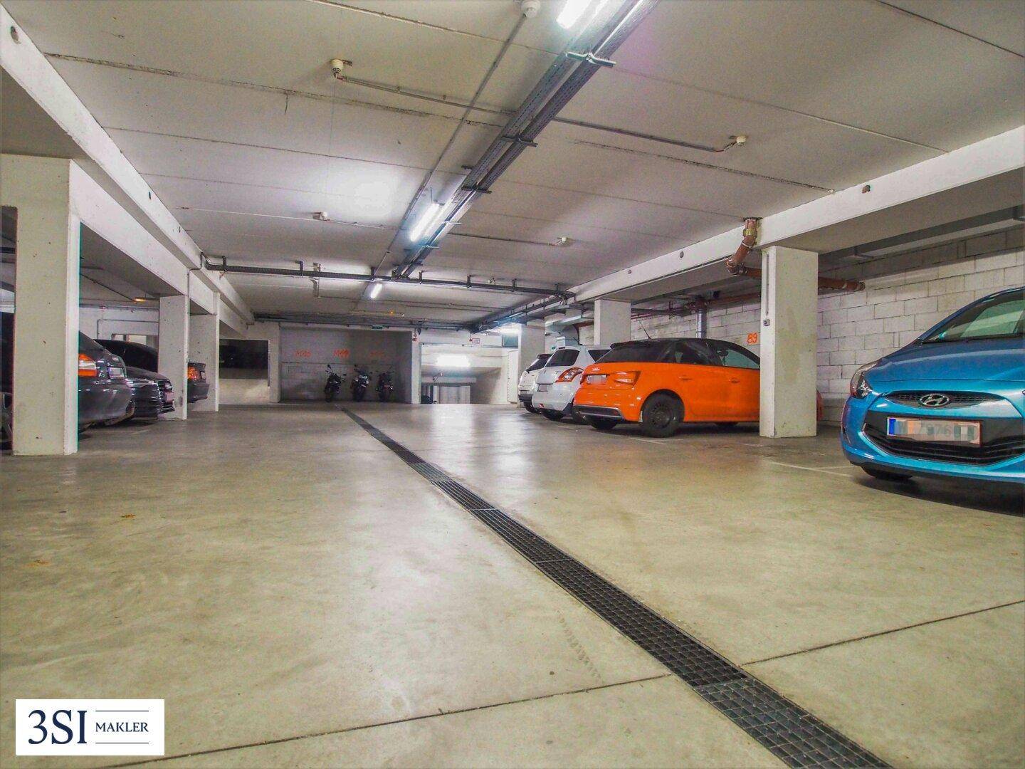 Helle Tiefgarage mit Betonboden und verschiedenen geparkten Autos, gut beleuchtet.