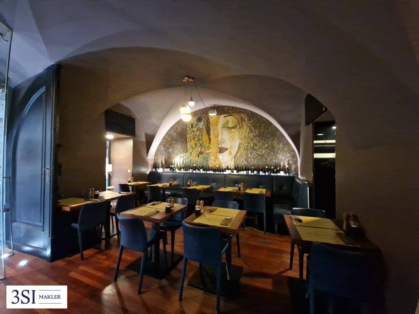 Gemütlicher Restaurantbereich mit gewölbter Decke, Holztischen und künstlerischer Wandmalerei.