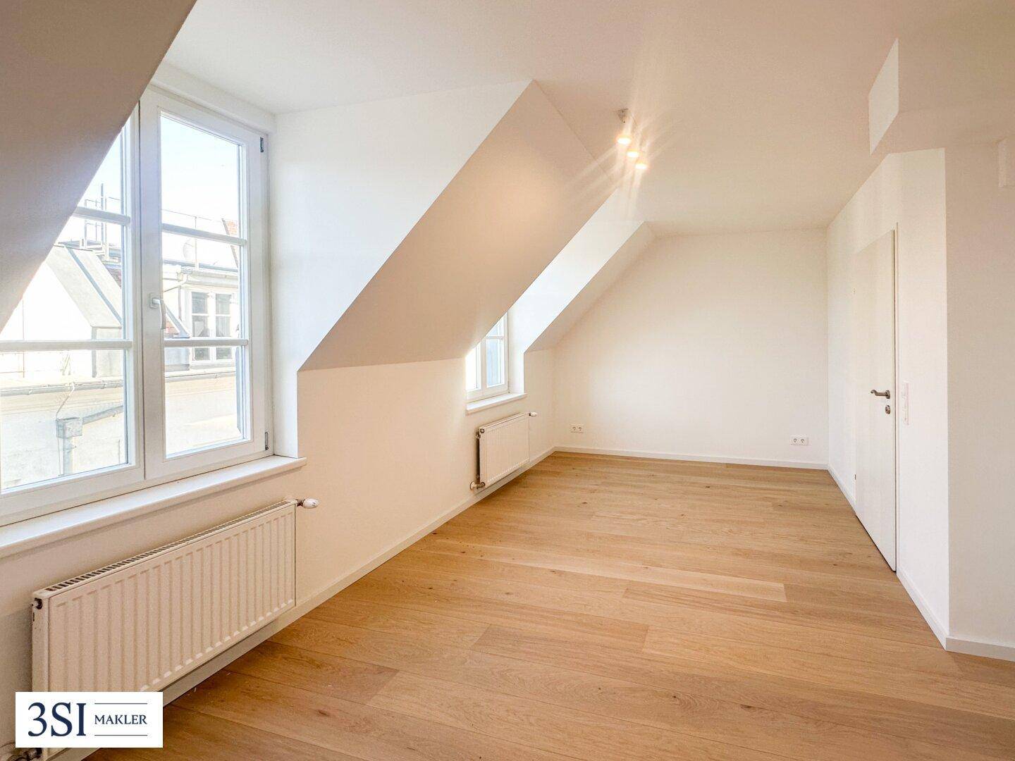 Heller Raum mit Holzboden, großen Fenstern und Dachschrägen, ideal als Schlafzimmer mit Einbauschrank.